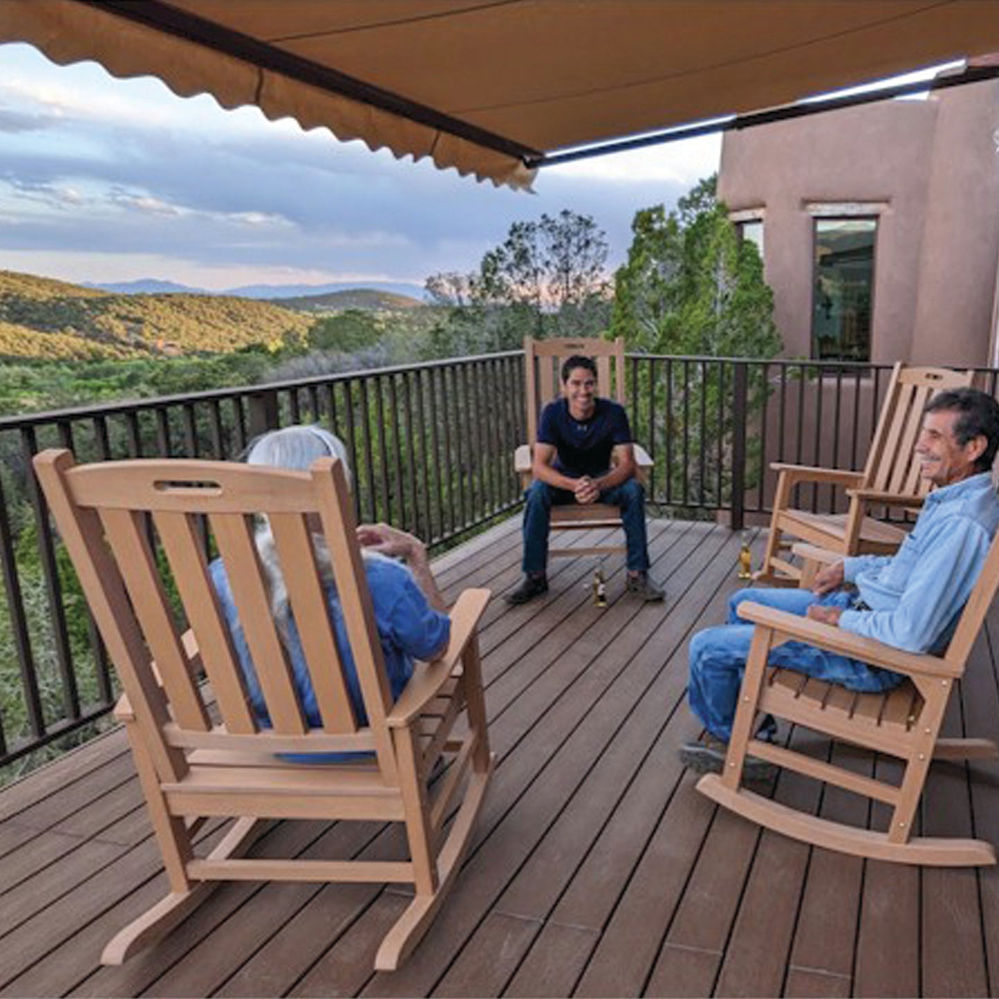 A013 Retractable Awning and Three people sitting on wooden rocking chairs on a deck with a scenic view of mountains and trees.