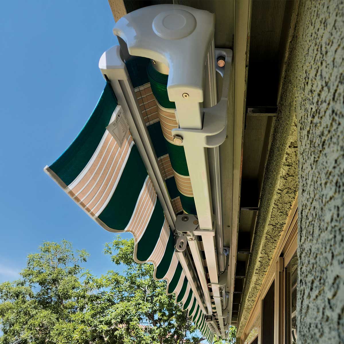 Green and white striped retractable awning on a building exterior with blue sky and trees in the background.